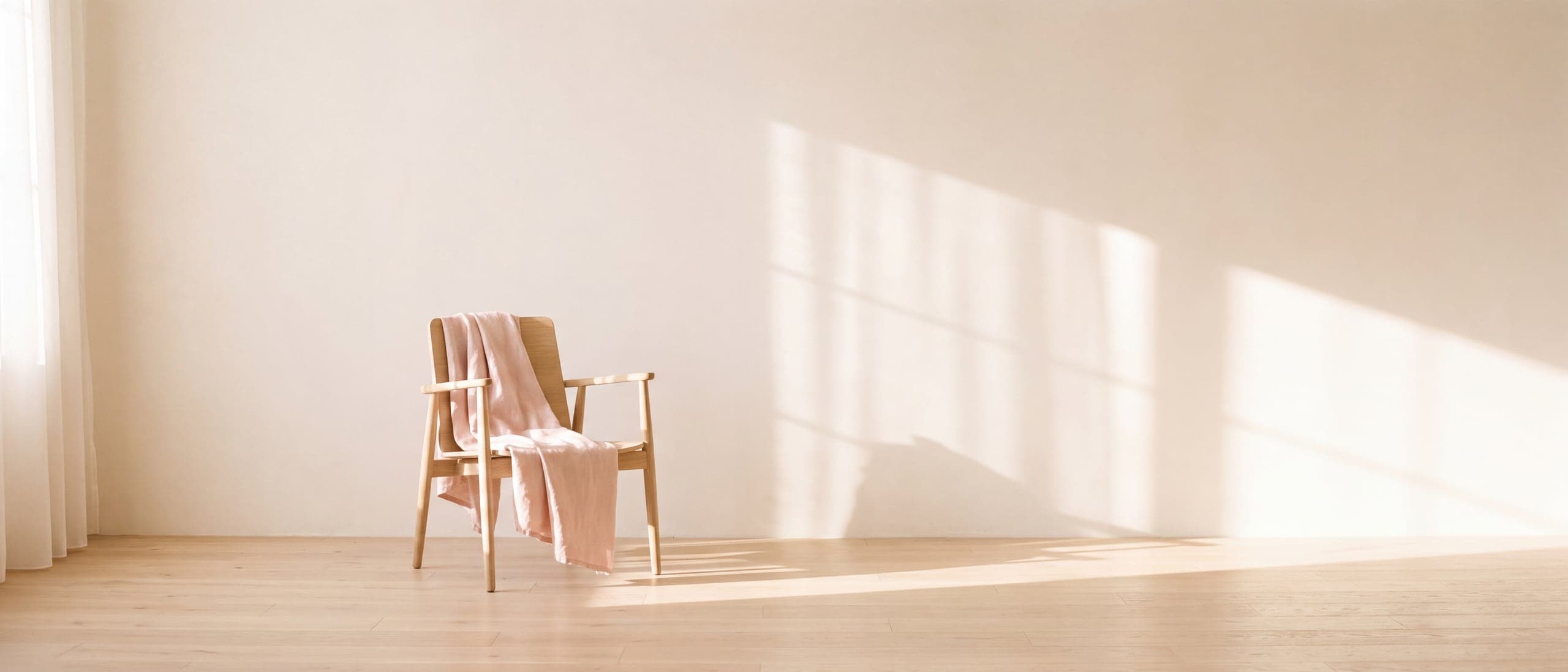 A pale oak chair with a soft blush linen throw, alone against a sunlit plaster wall