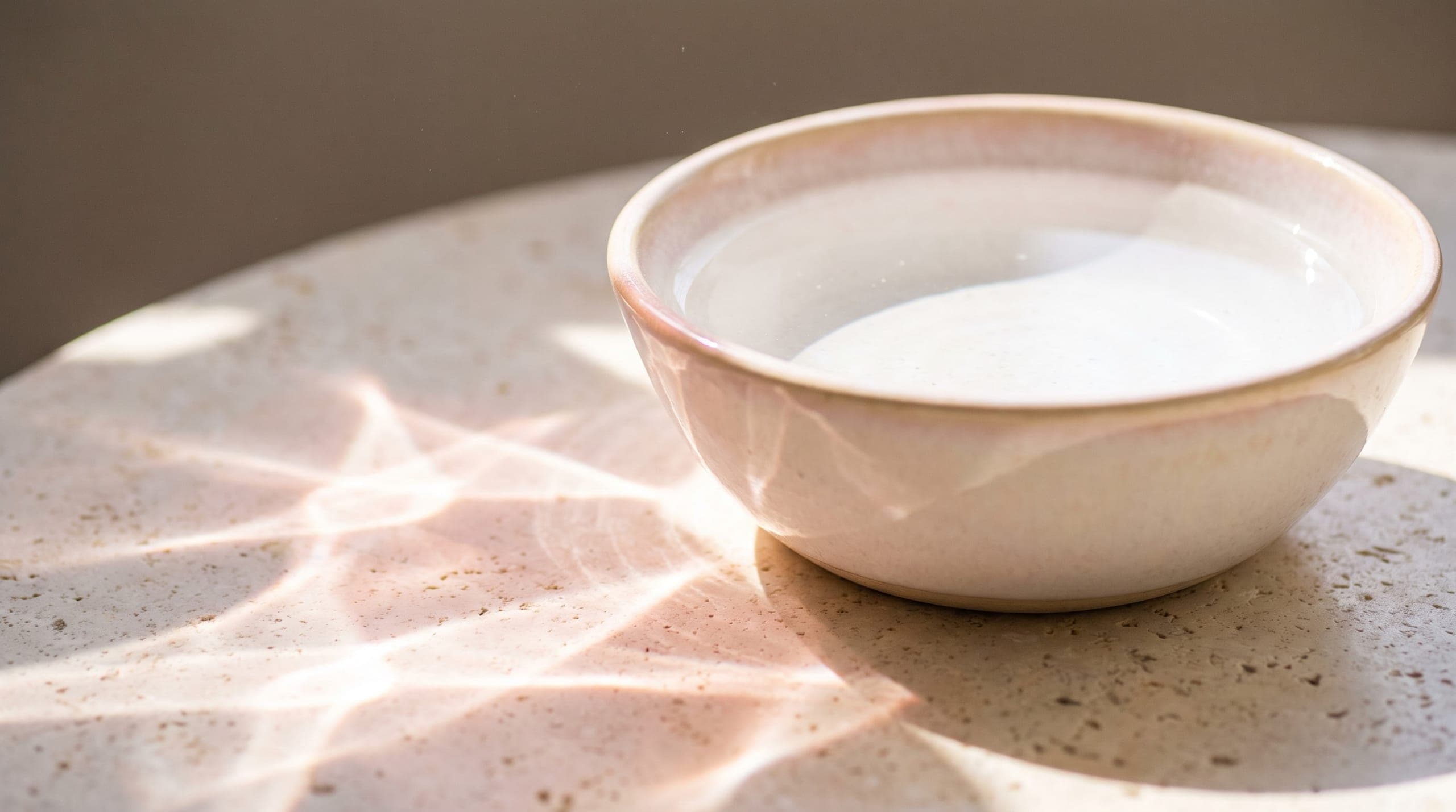 Water in a pale ceramic bowl, throwing caustic light across a cream surface.