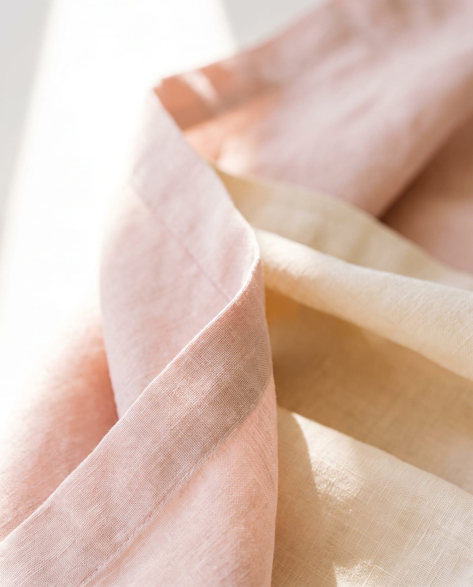 Soft blush and cream linen in gentle overlapping folds, lit from the side by clean daylight.